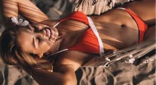 Woman lying in a hammock on a sandy beach.