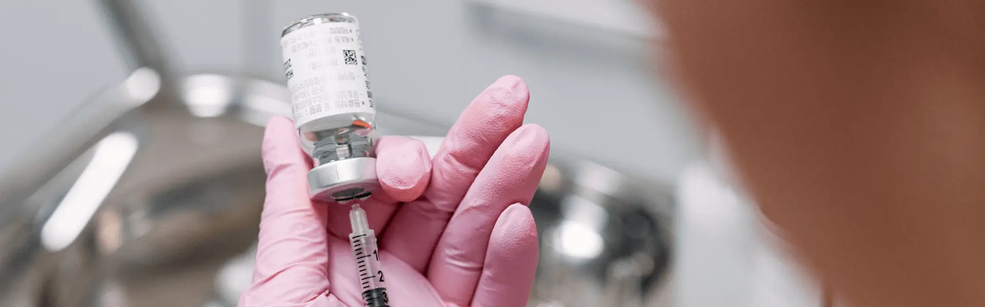 A woman in pink gloves is holding a syringe.
