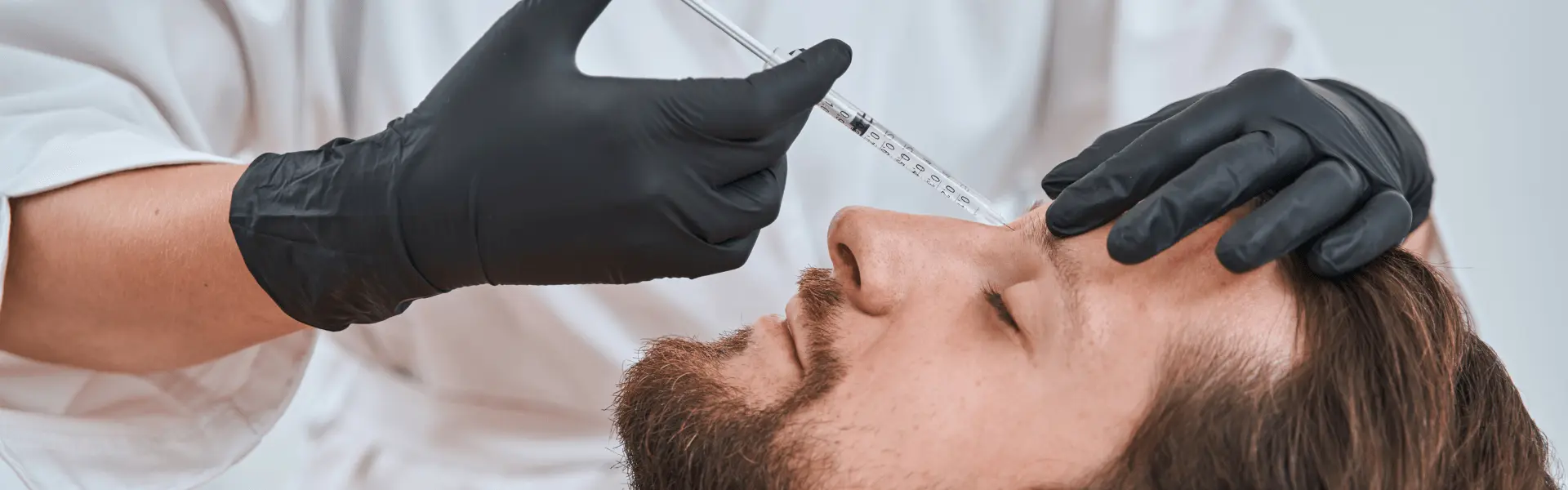 A man in black gloves getting a beard injection.