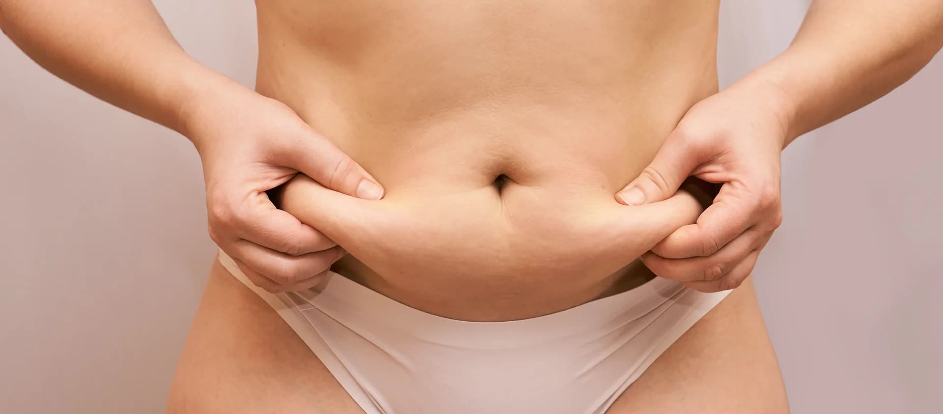 A close-up of a person pinching belly fat while wearing white underwear against a neutral background, indicative of areas targeted by Lipo 360.