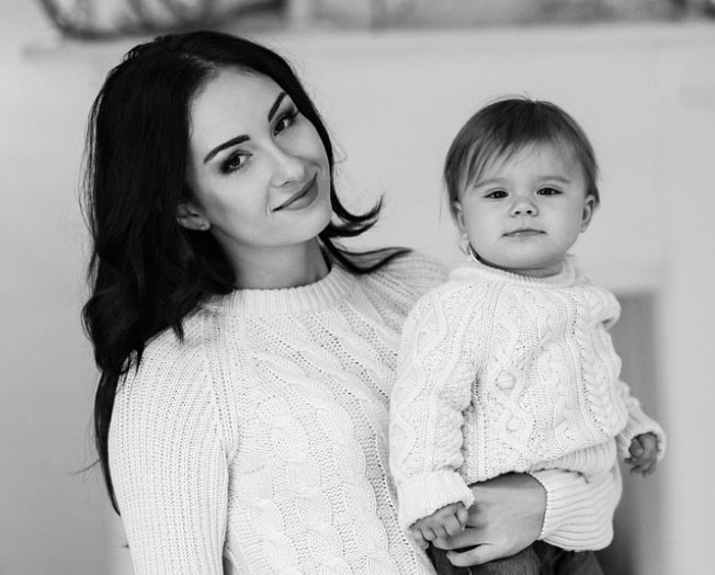 Black and white photo of a woman holding a baby in a cozy sweater, radiating the purest love for her child.