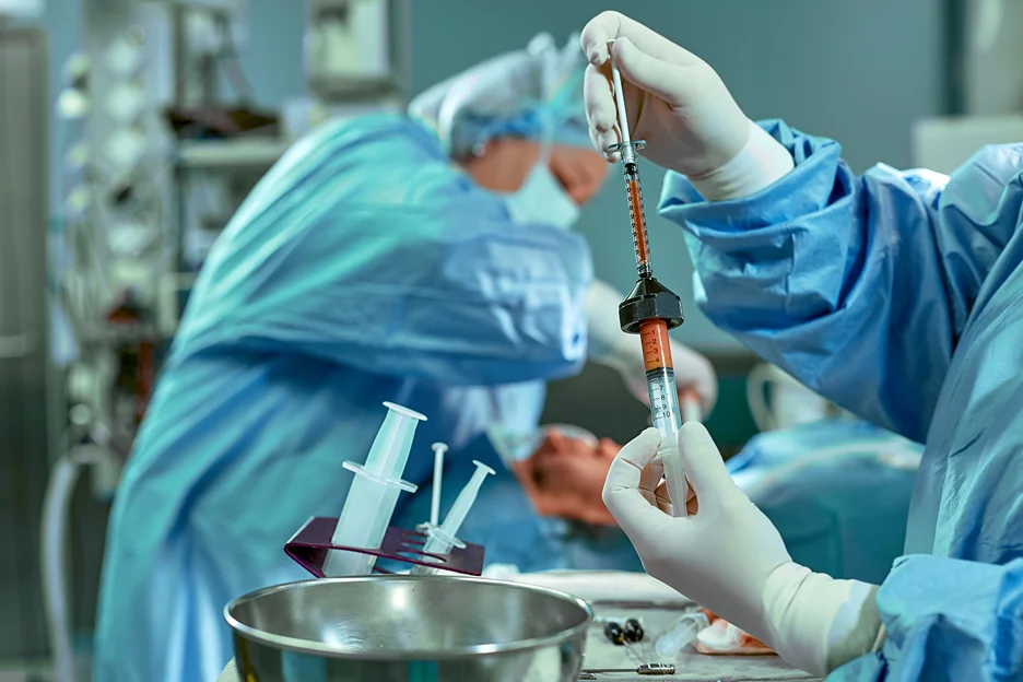 A group of surgeons  holding a syringe with fat in an operating room.
