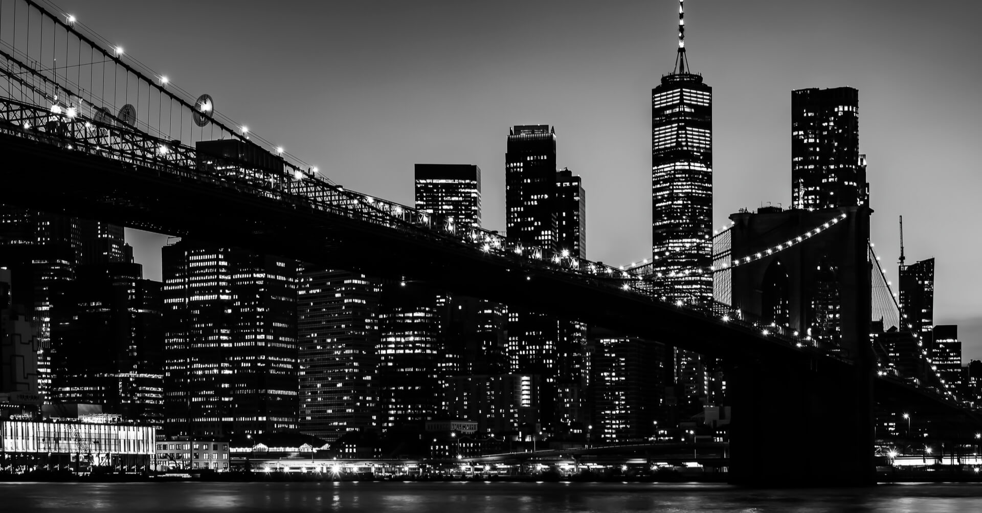 Black and white photo of the brooklyn bridge at night.