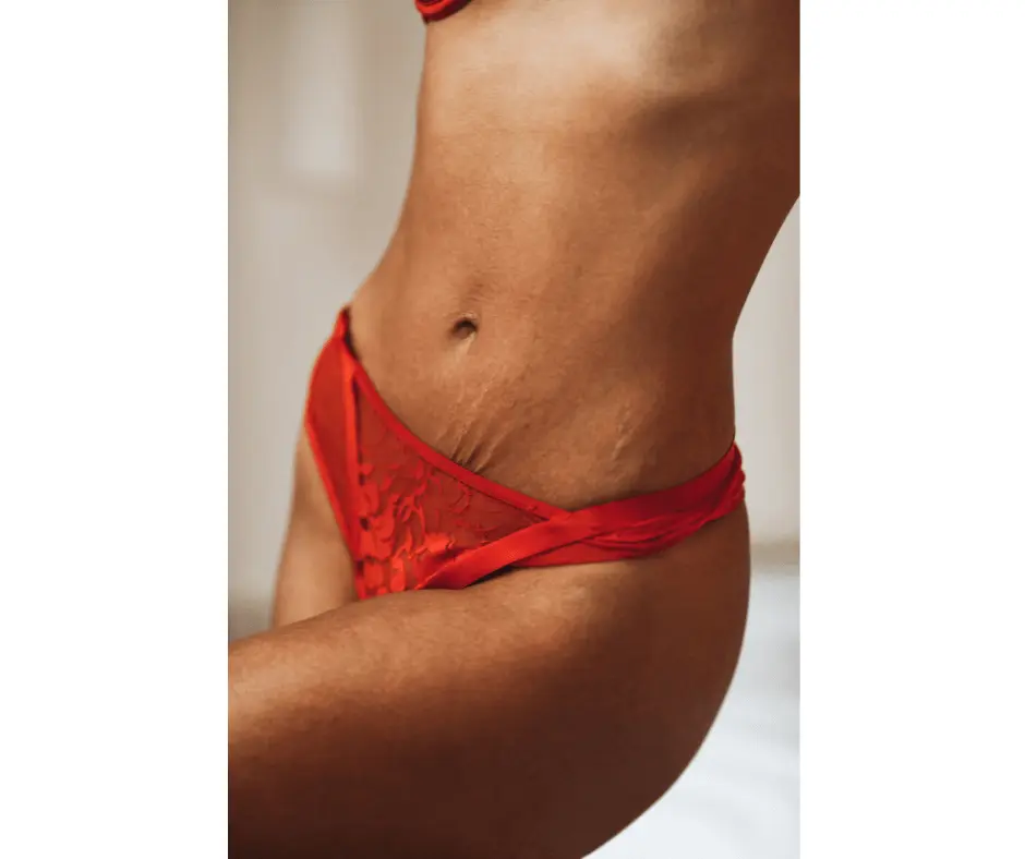 A woman in red lingerie showcasing her toned abdomen while posing on a bed.