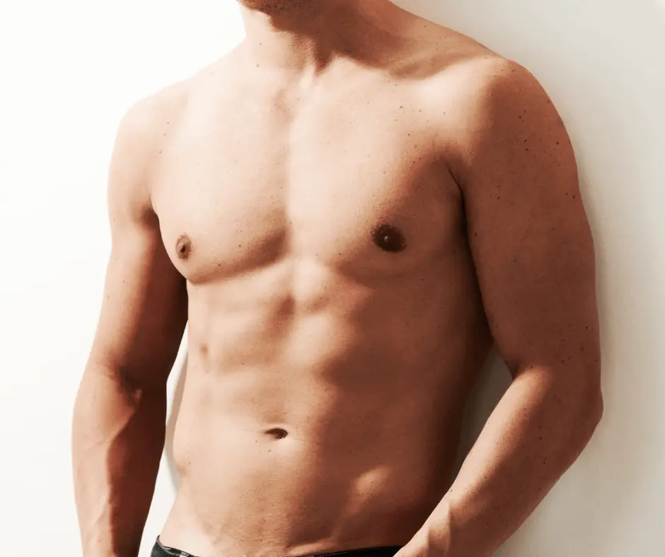 A shirtless man showcasing his defined abdomen as he casually leans against a wall.