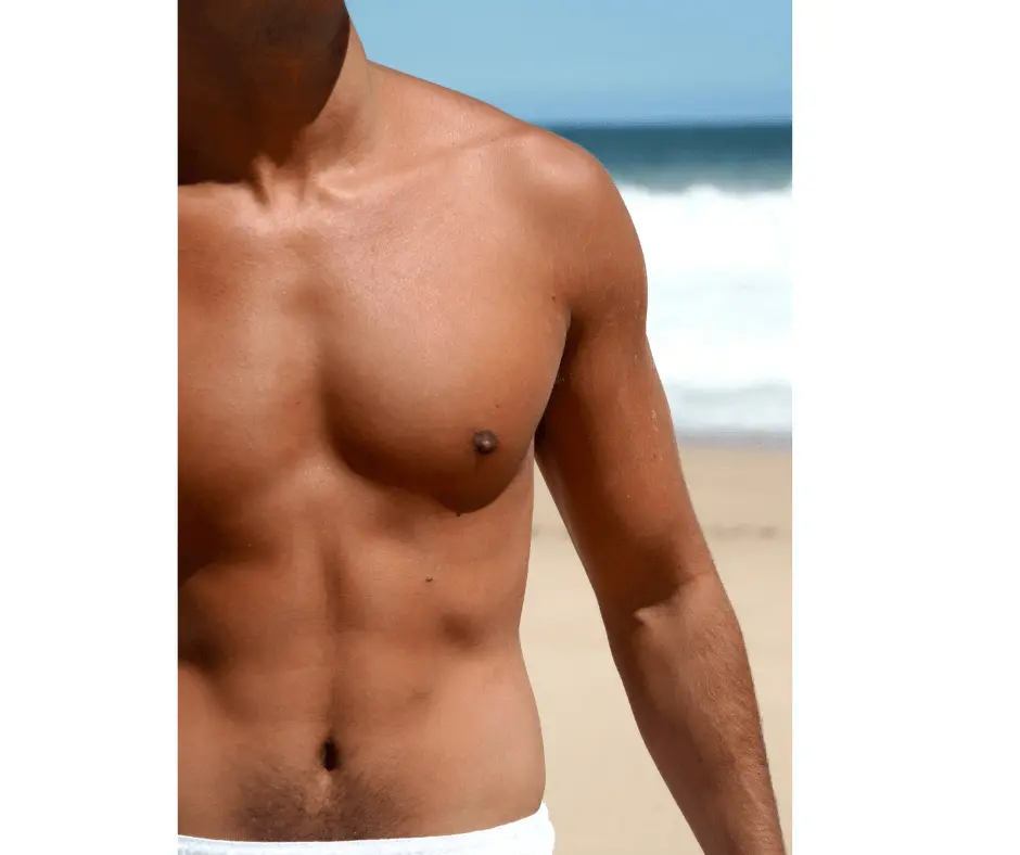 A shirtless man is standing on the beach, proudly displaying his well-toned abdomen.