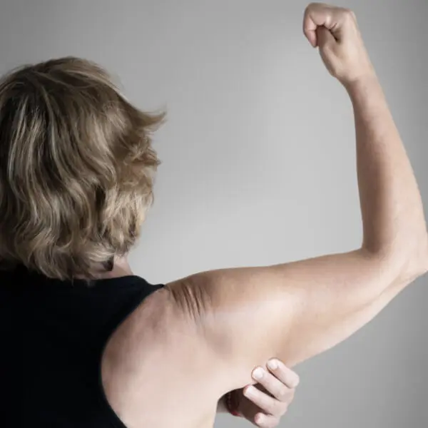 A woman flexing her arms in front of a gray background.