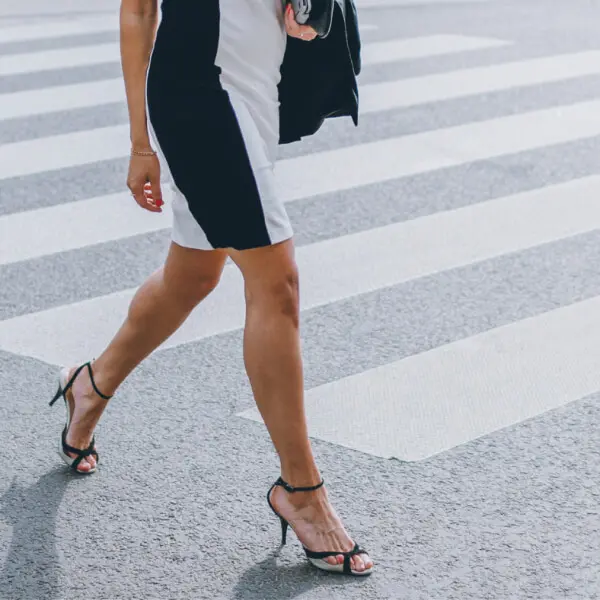A woman in a black and white dress crossing the street, showcasing her toned calf.