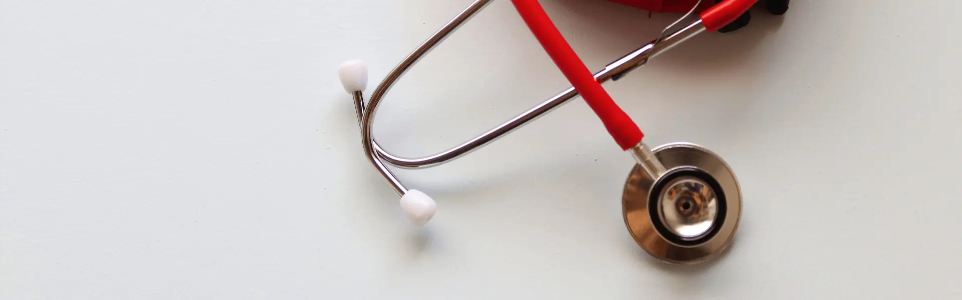 A red stethoscope hanging on a white wall.