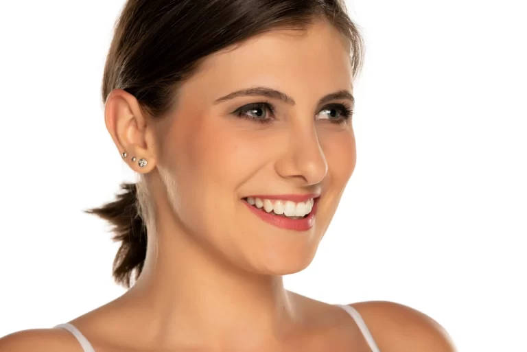 A woman smiles while wearing a white tank top, showcasing her dream jawline after chin and jowl liposuction.