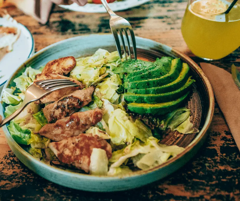 A large plate of salad with chicken and avocado on a wooden table.