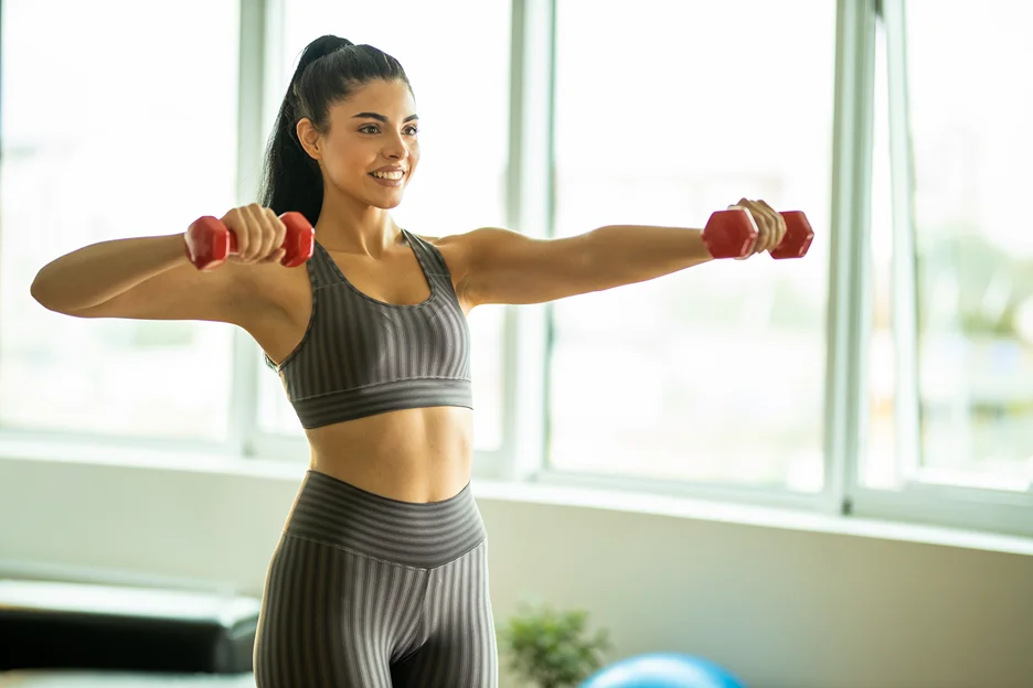 A woman carefully lifting dumbbells in a gym.