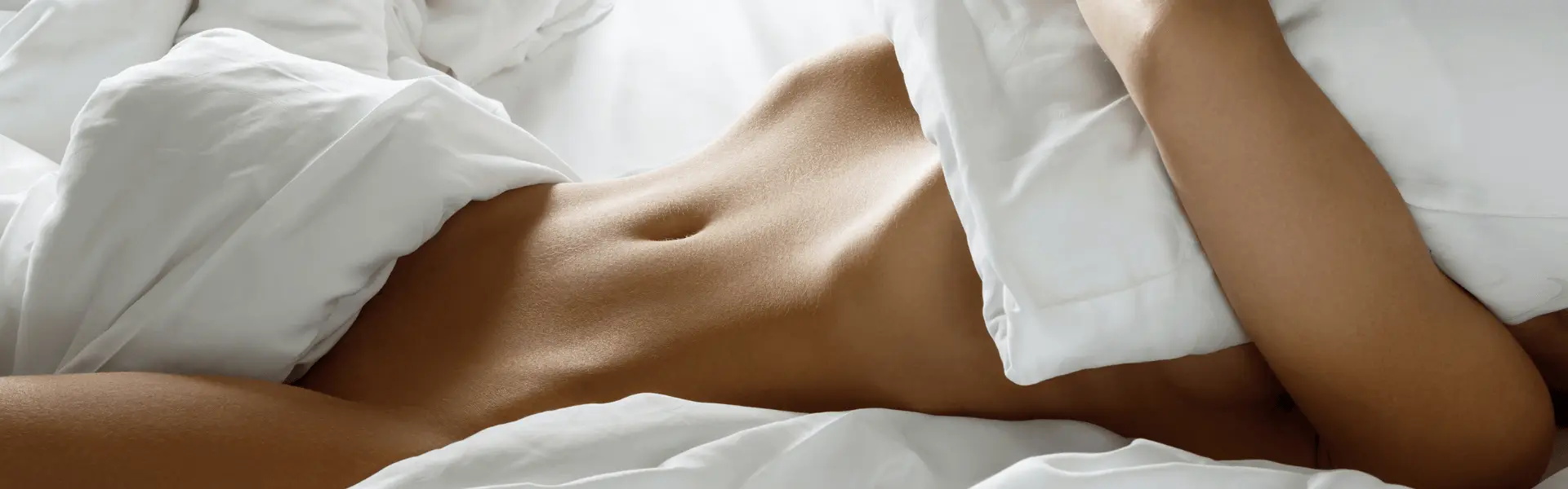 A naked woman laying on a bed with white sheets.