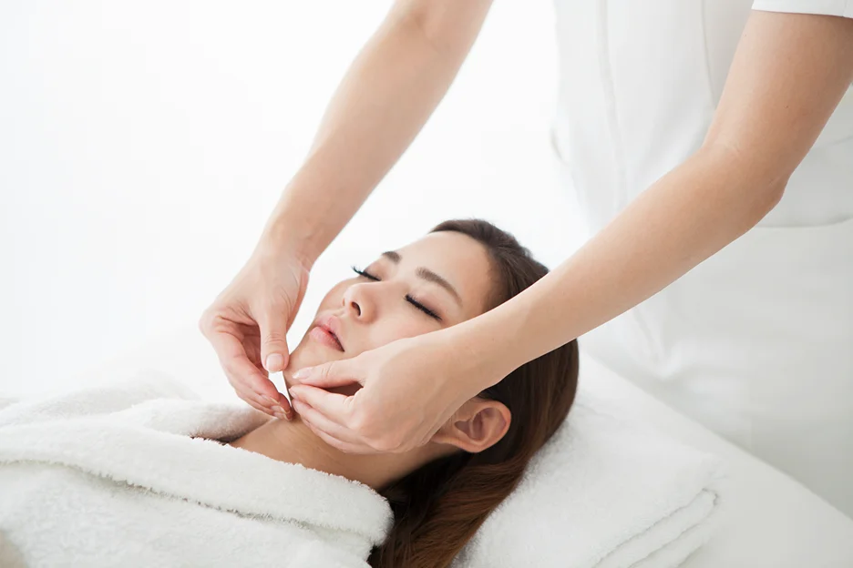 A woman receiving a facial massage at a spa, targeting swollen lymph nodes.