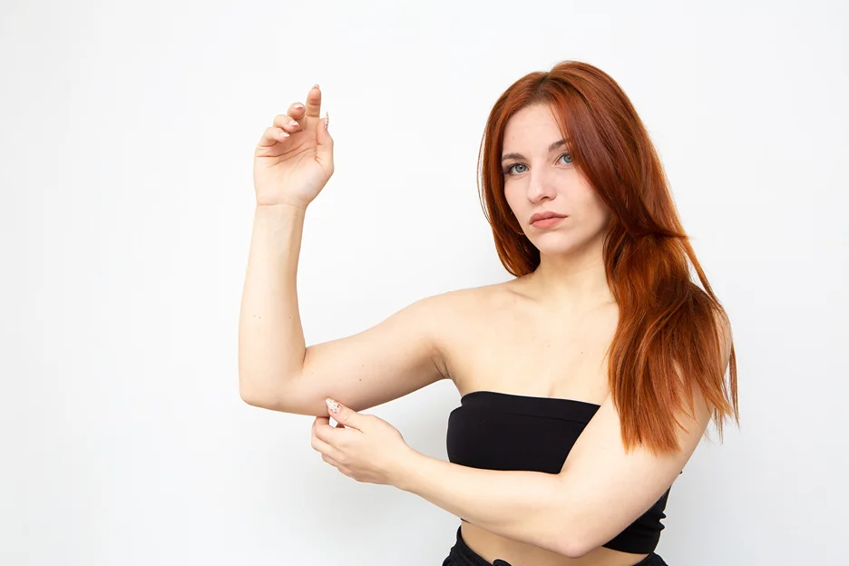 A woman with red hair pointing to her arm after arm contouring procedure.