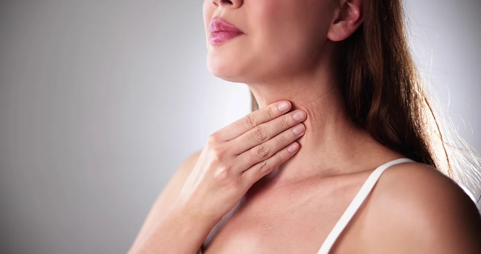 A woman is gently touching her neck with her hand, focusing on the delicate area beneath her chin.