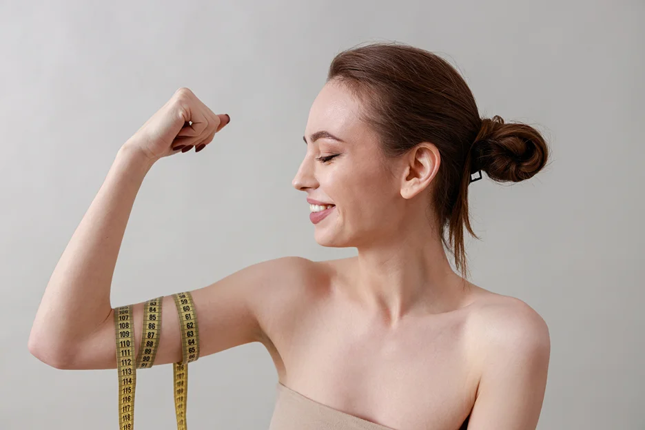 A woman flexes her arm while holding a measuring tape.