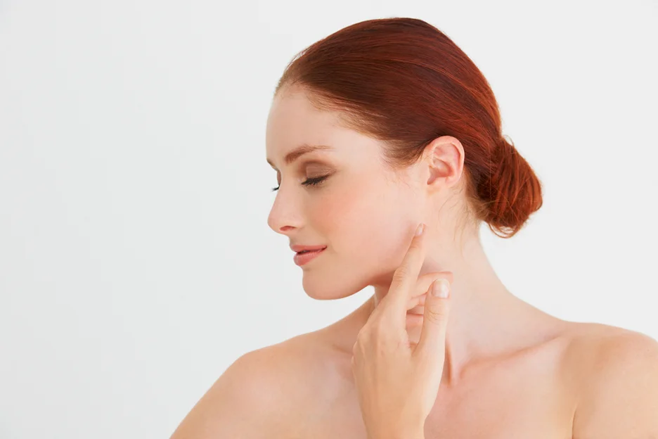 A woman with red hair is touching her face with her finger, showing off her defined jawline.
