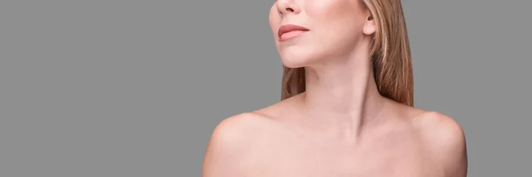 A woman is shown in a gray background post chin liposuction to define her ideal jawline.