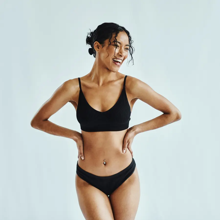 A woman in a black bikini posing for a photo, showcasing her flat stomach.